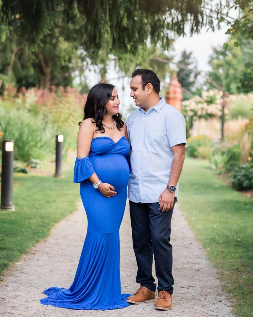 An expectant couple walking along a sun-dappled garden path during their professional maternity photo session in the GTA.
