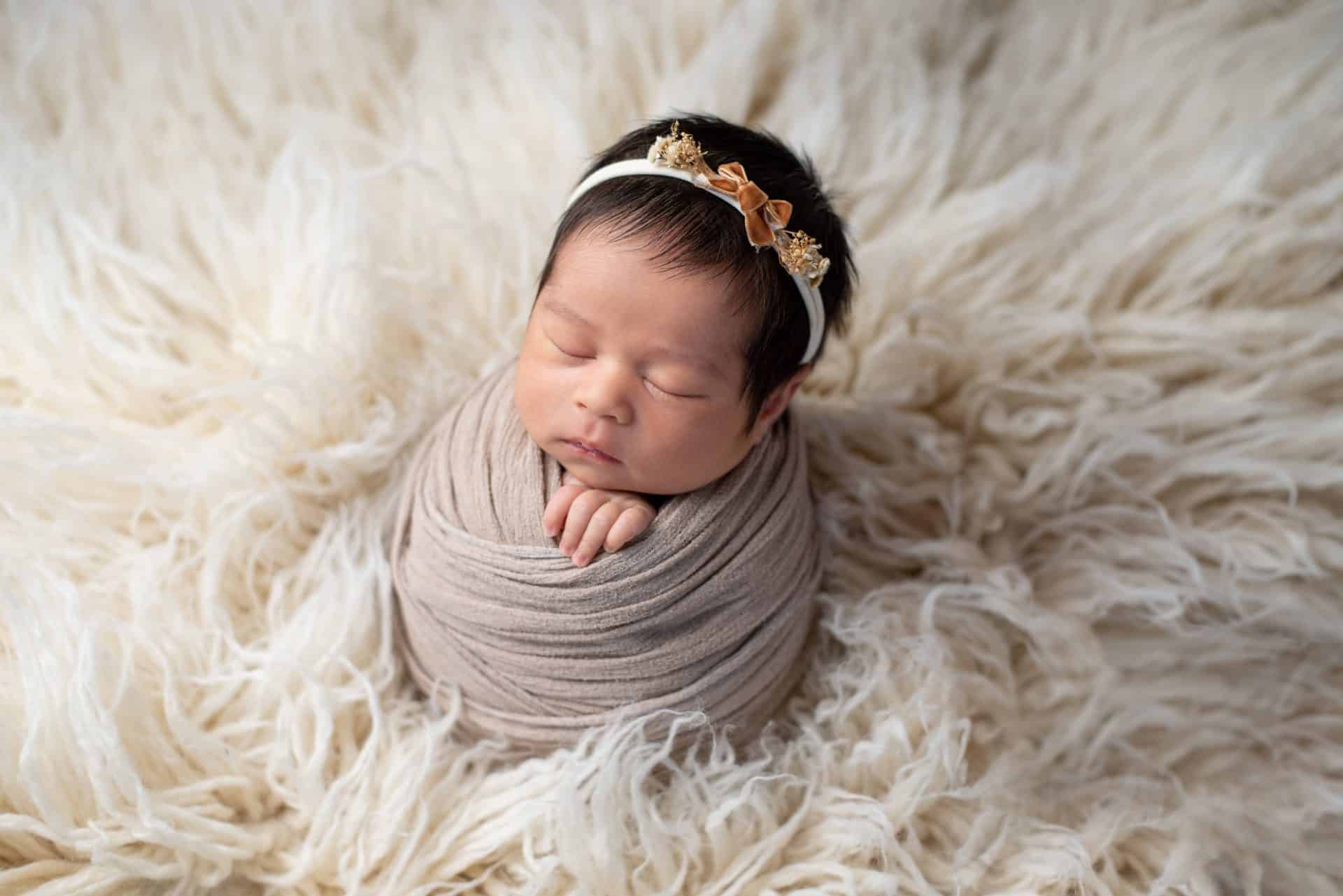 Dreamy newborn baby sleeping on a fluffy white blanket, wrapped in grey with a headband, perfect for a luxury newborn photography Mississauga session