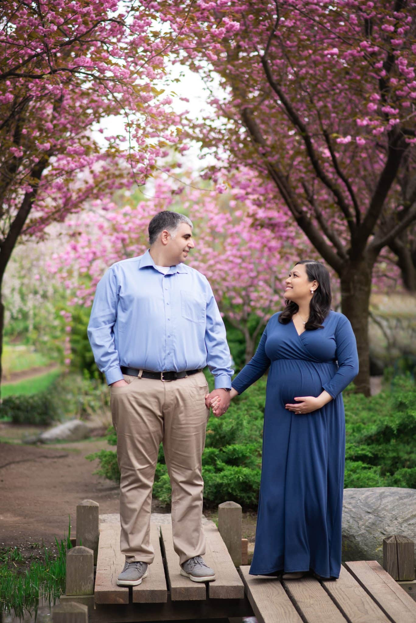 Maternity photography session with couple walking under blooming cherry blossom trees, outdoor pregnancy photoshoot in Toronto park setting.