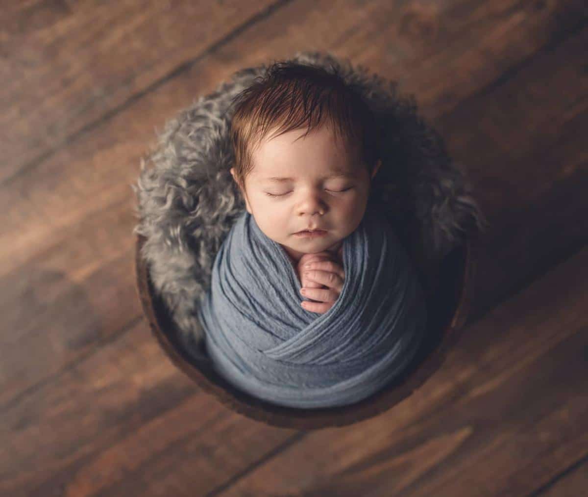 Sleeping newborn wrapped in a soft blue swaddle in a wooden bowl during a newborn photography Toronto session