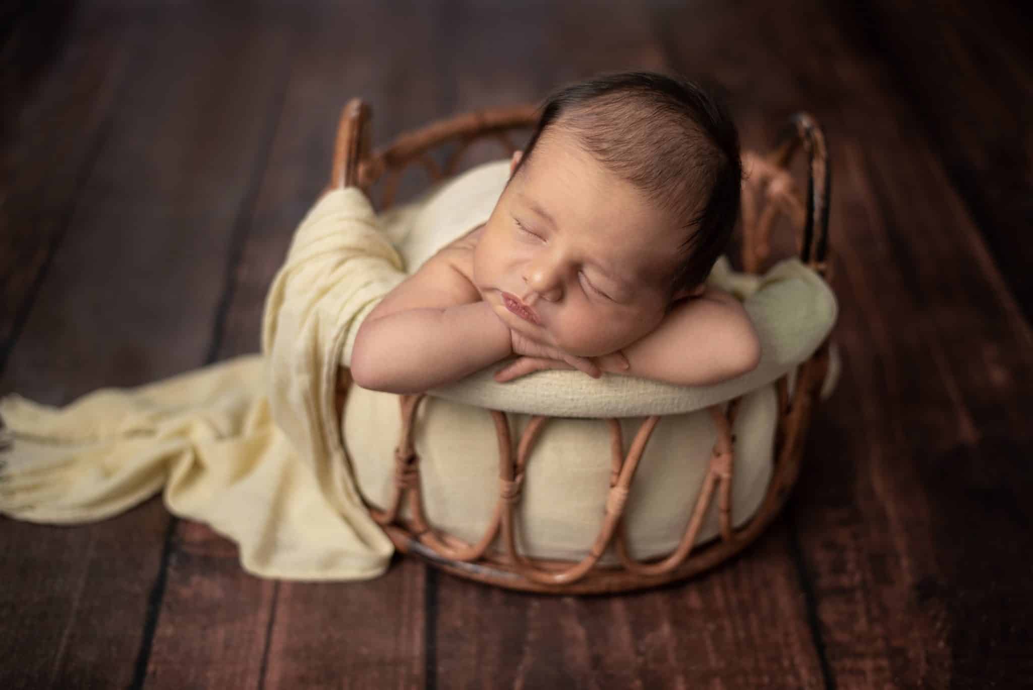 Charming newborn baby sleeping in a basket with a light green wrap, ideal for a newborn photo session Mississauga