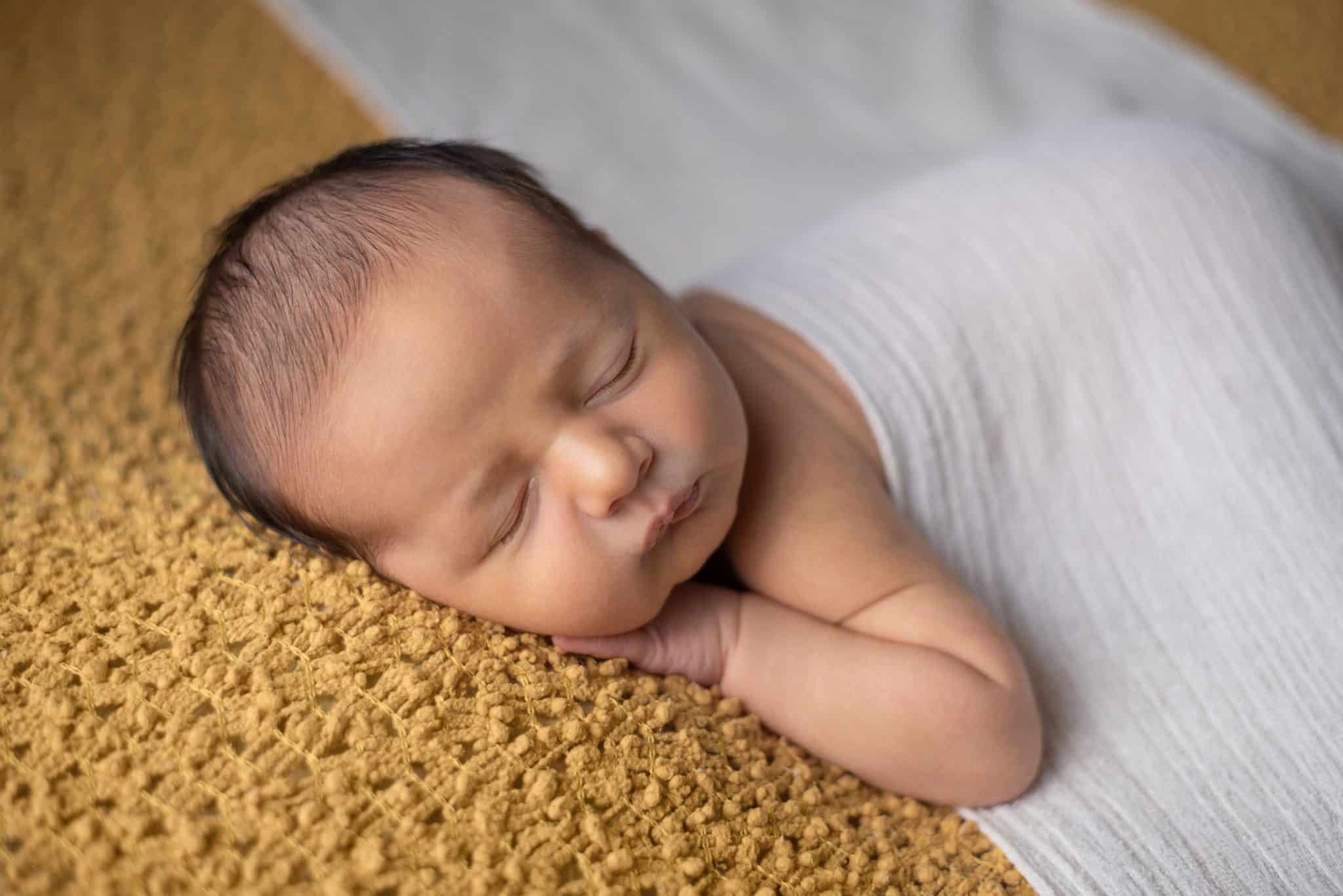 Serene newborn baby sleeping on a textured yellow backdrop, showcasing professional newborn photography Mississauga.