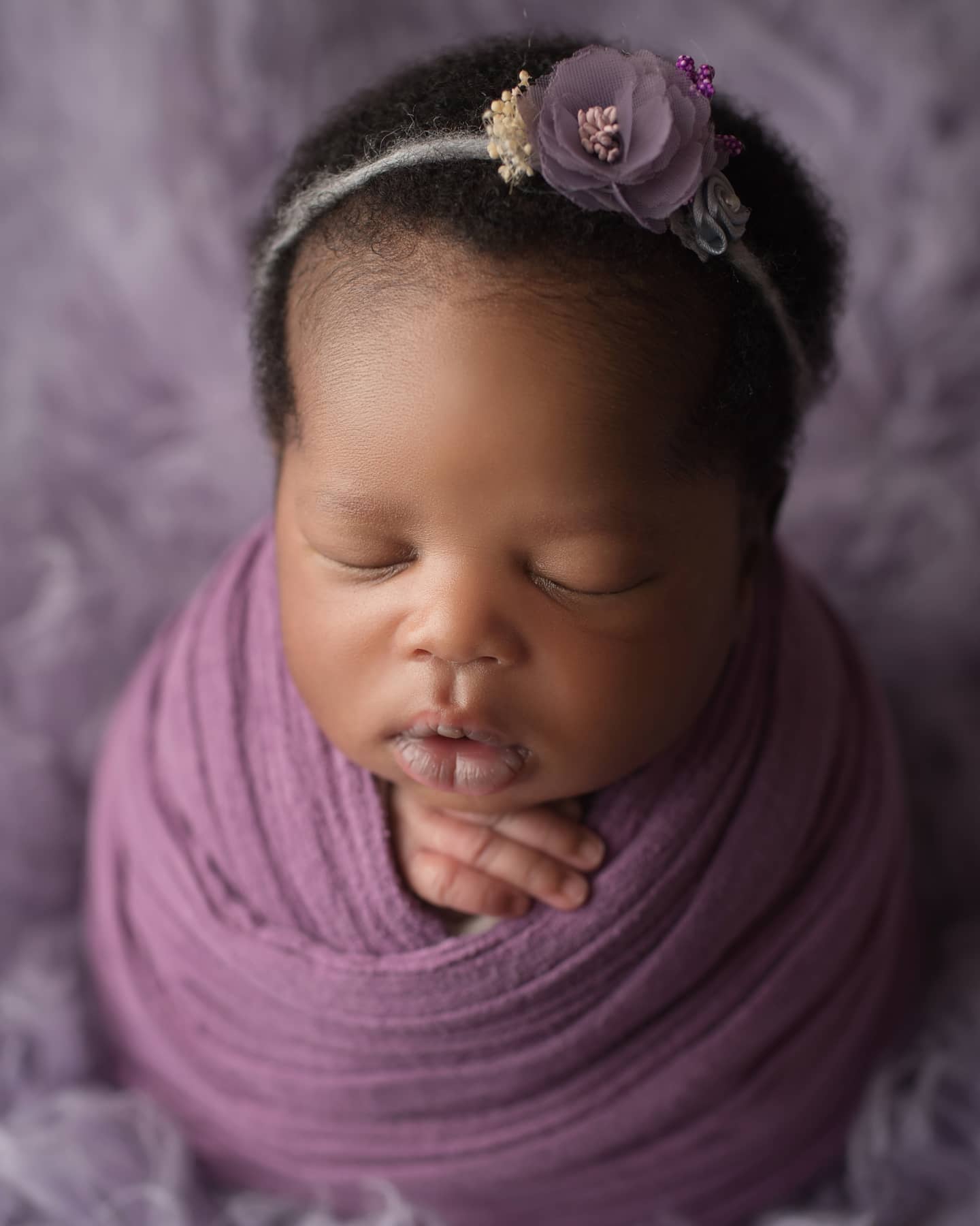 Sleeping newborn baby girl wrapped in purple with a floral headband, captured by a professional newborn photographer Mississauga.