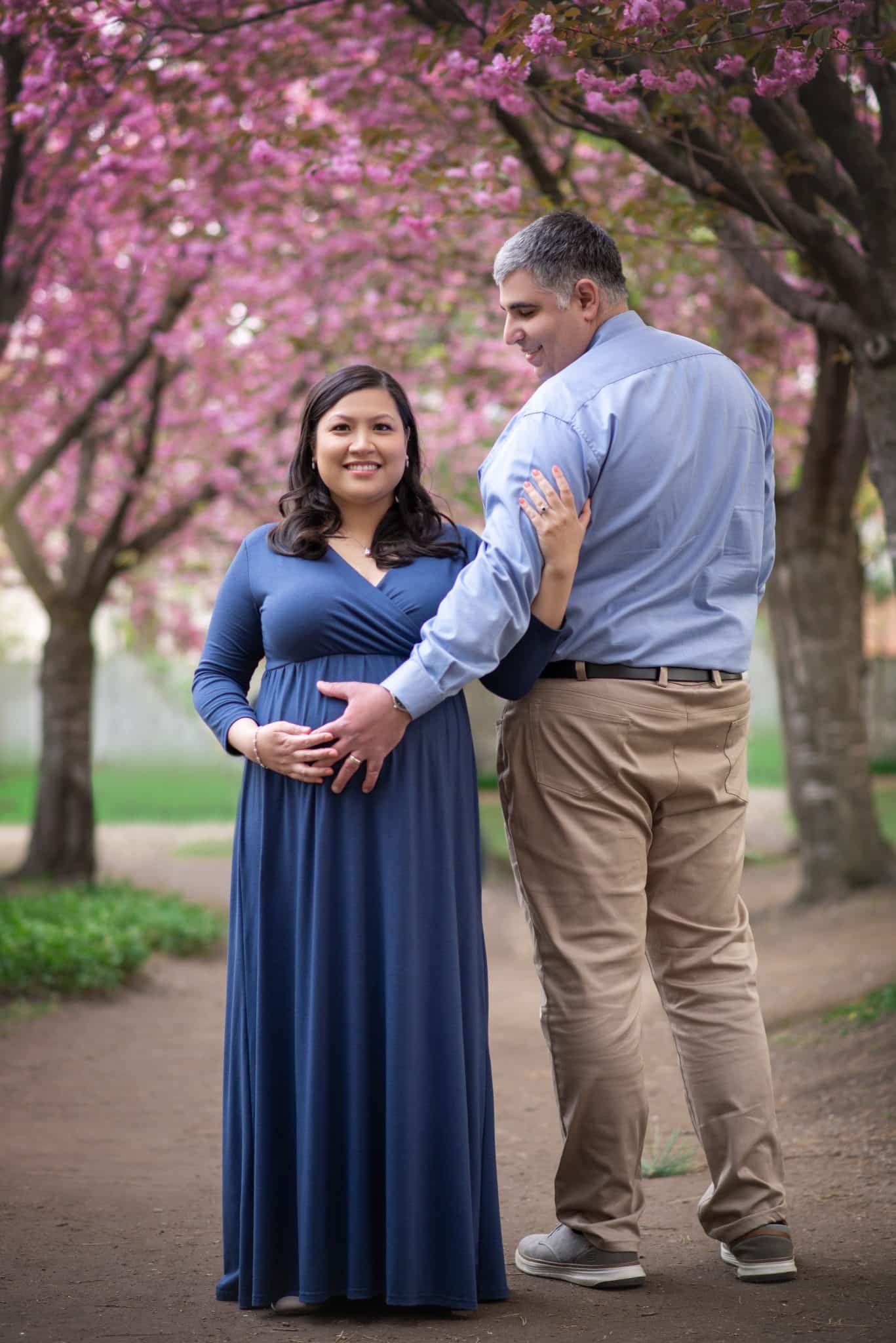 Pregnant couple maternity photoshoot under cherry blossoms, outdoor pregnancy photography in Toronto park, romantic spring engagement style session.