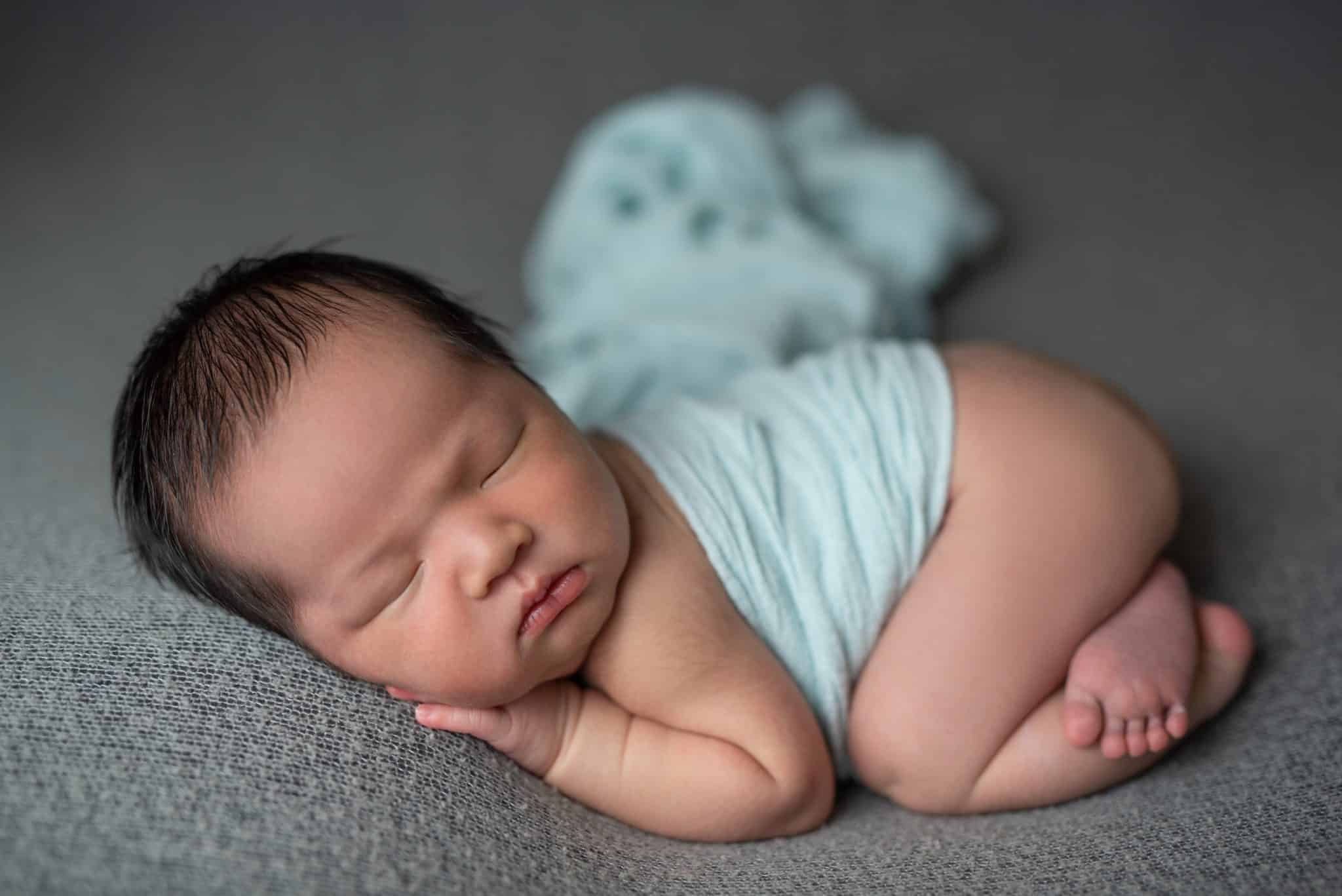 Minimalist Toronto newborn photography of sleeping baby wrapped in soft beige fabric on neutral backdrop