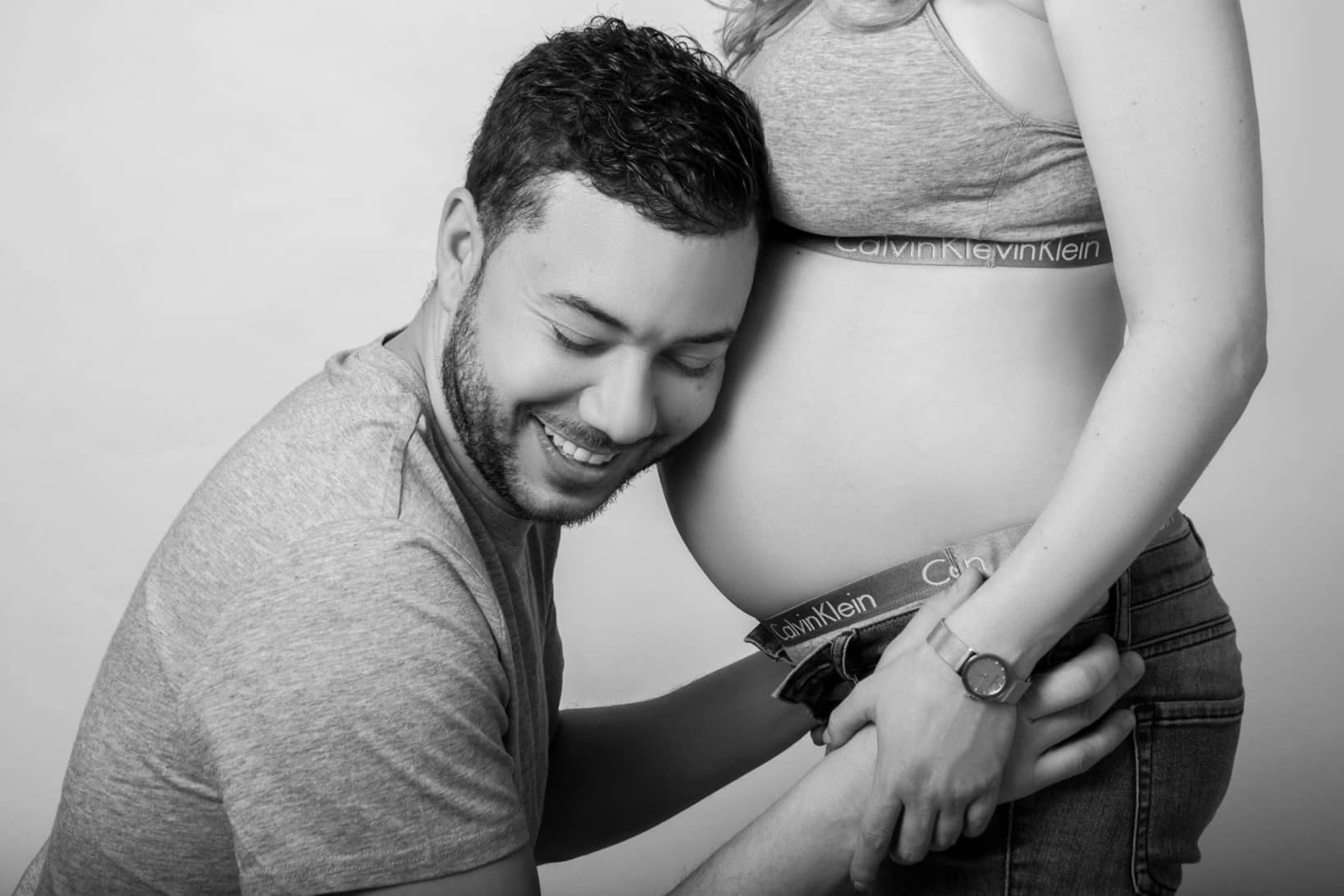 A black and white close-up of a man leaning his head against his partner's pregnant belly during an intimate maternity photo session in Toronto.