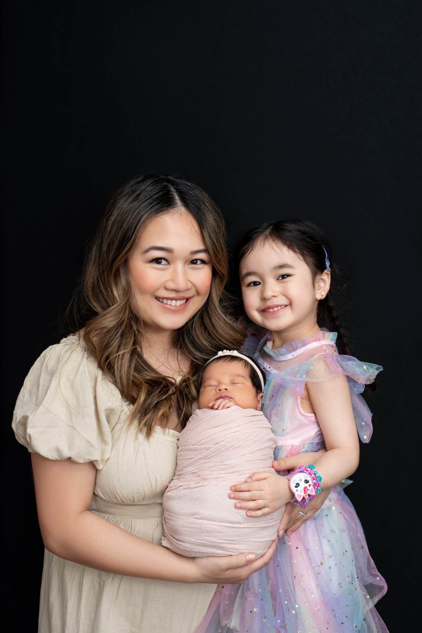 Mother holding her newborn baby with older sister during a warm family newborn photography Toronto portrait