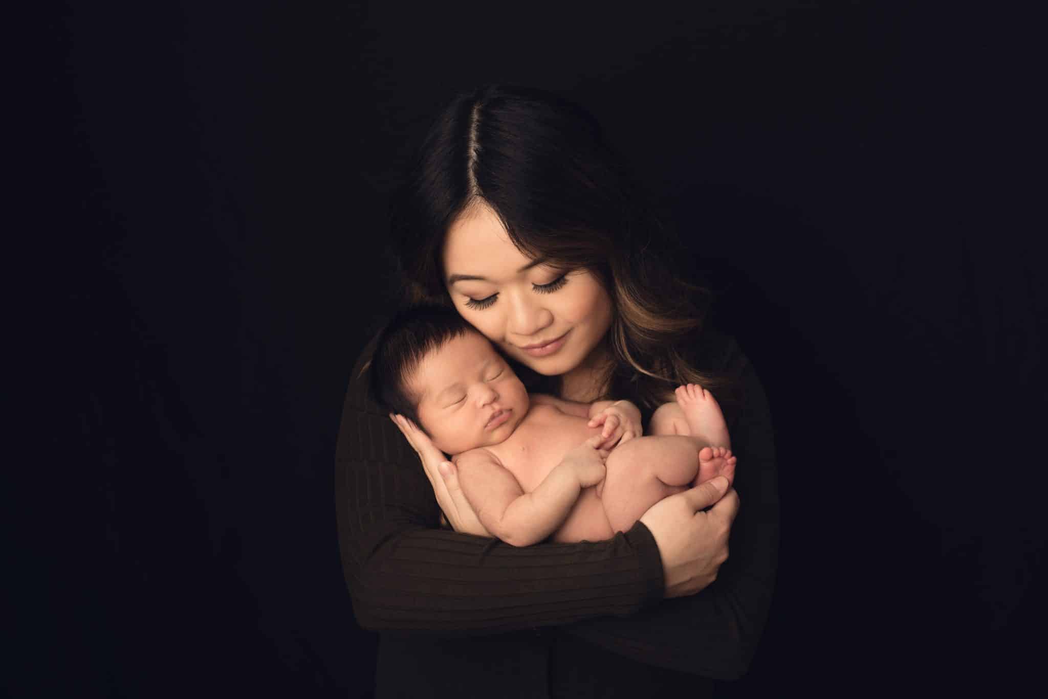 Best newborn photographer Toronto – mother holding sleeping newborn in intimate dark studio setup