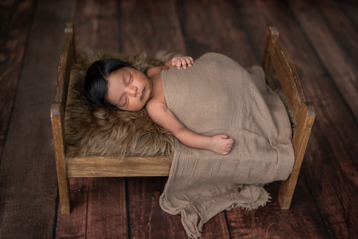 Peaceful newborn baby sleeping in a rustic wooden bed, perfect for a newborn photoshoot Mississauga