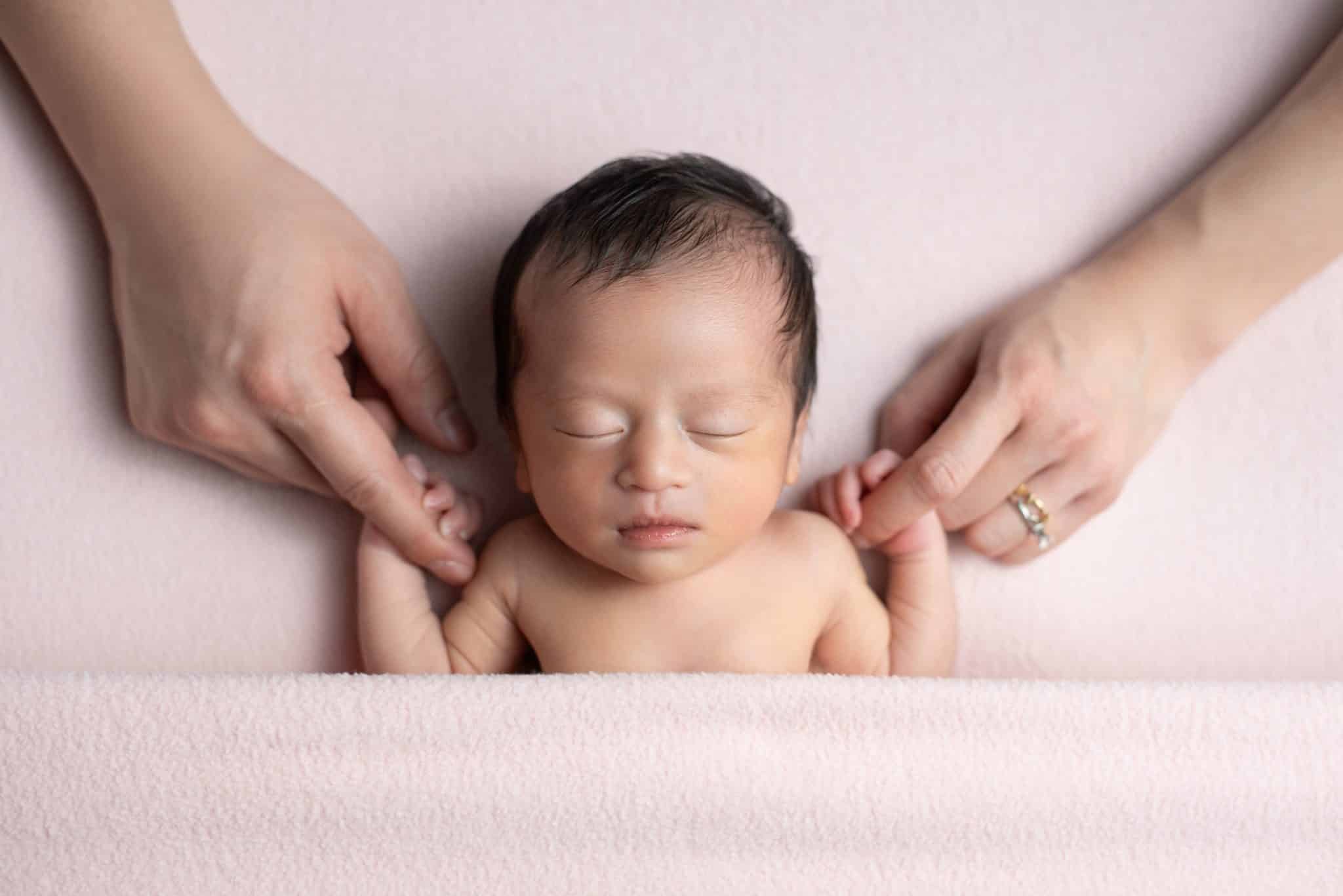 Natural newborn portrait with baby softly posed and supported by parents’ hands during a newborn photography Toronto session