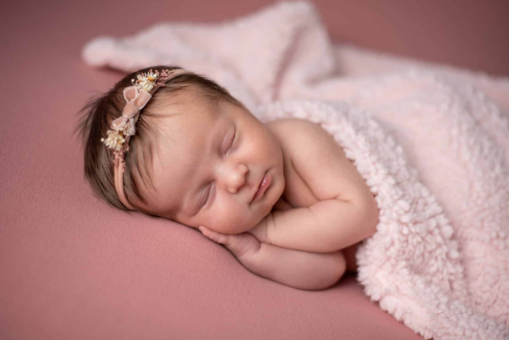 Newborn baby girl sleeping on a soft pink blanket during a cozy newborn photography Toronto session