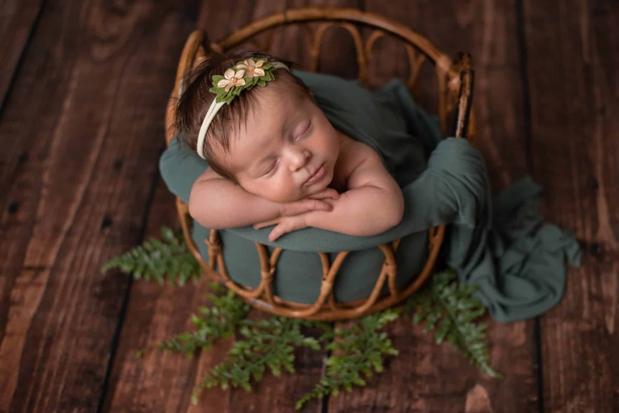 Sleeping newborn girl in a basket with greenery accents captured by a Toronto newborn photographer