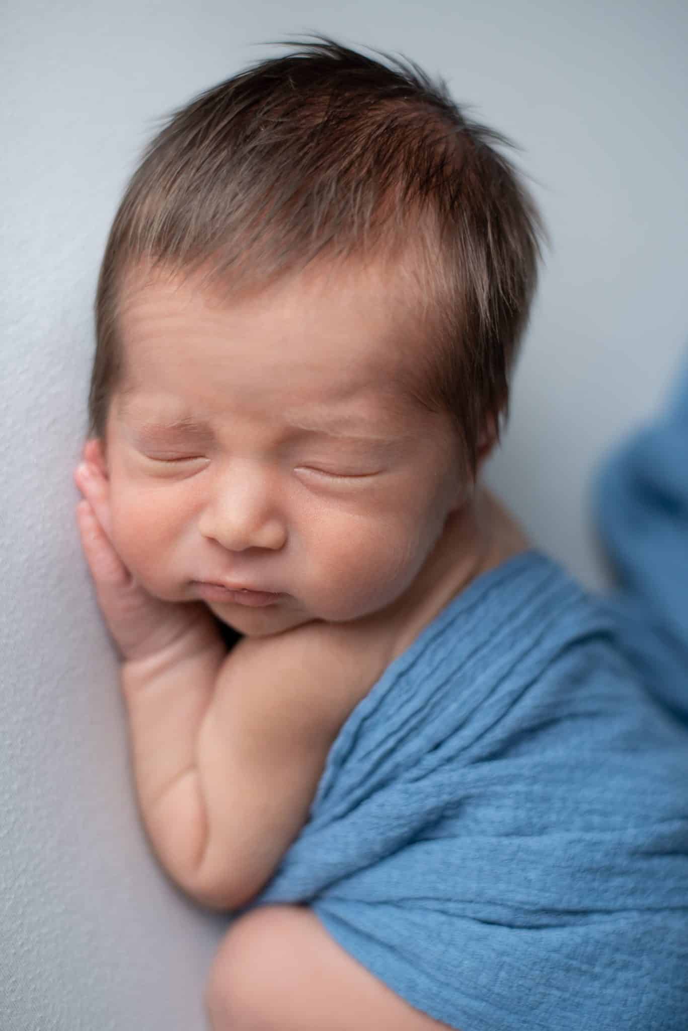 Close-up of a serene newborn baby sleeping, wrapped in blue, highlighting the detail in newborn photography Mississauga.