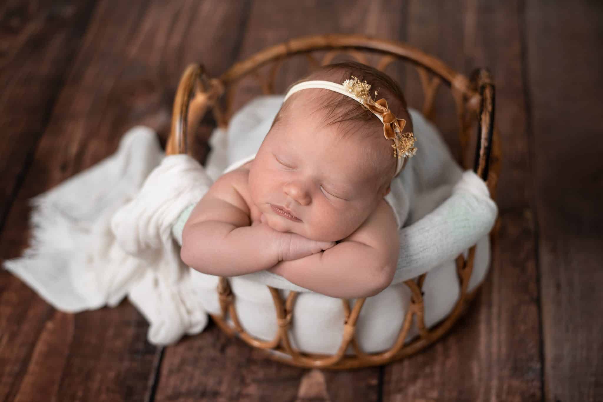 Peacefully sleeping newborn posed in a cozy basket with white wrap photographed by a Toronto newborn photographer