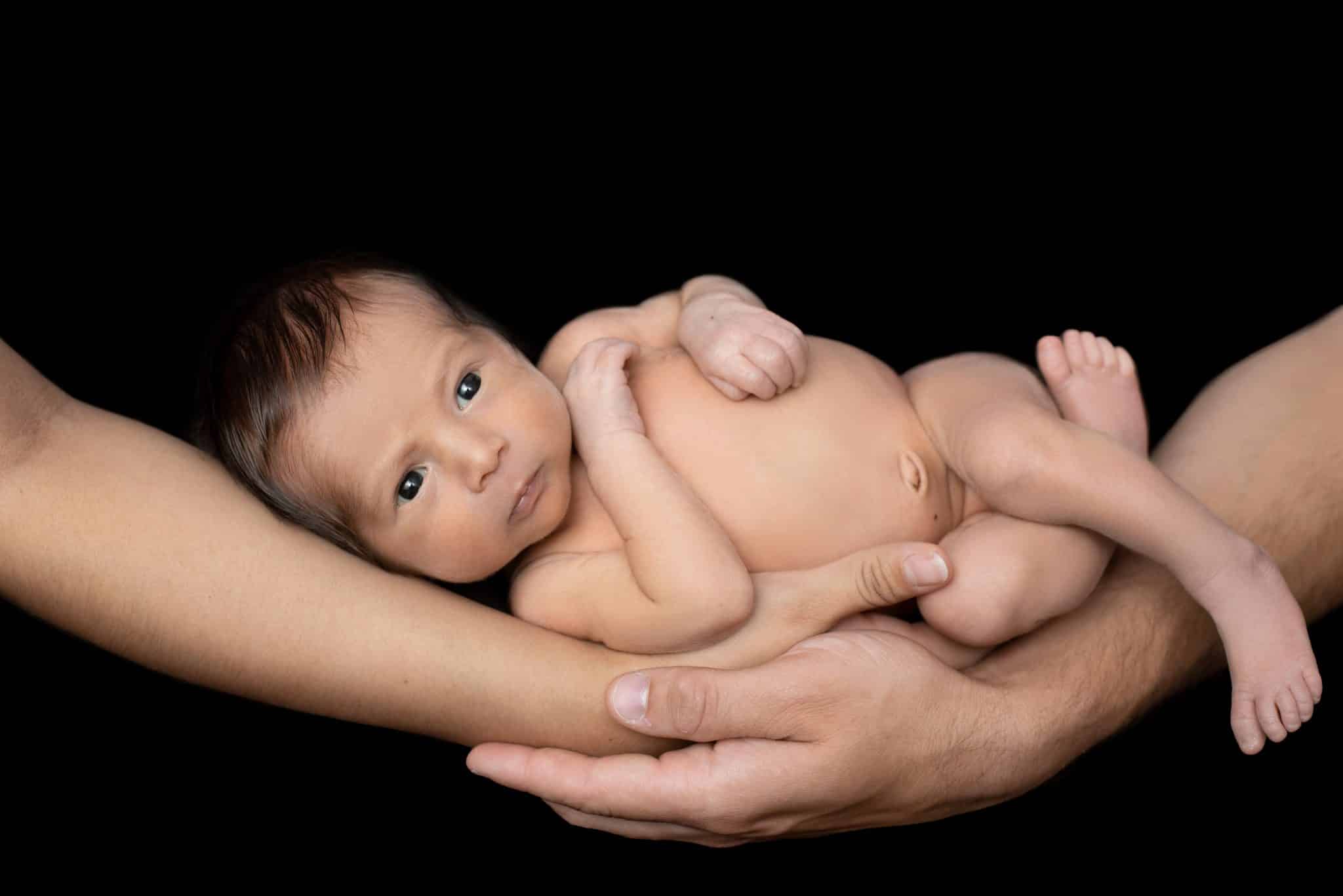 Tender moment of a newborn baby held in loving hands, showcasing the care of a newborn photographer Mississauga.