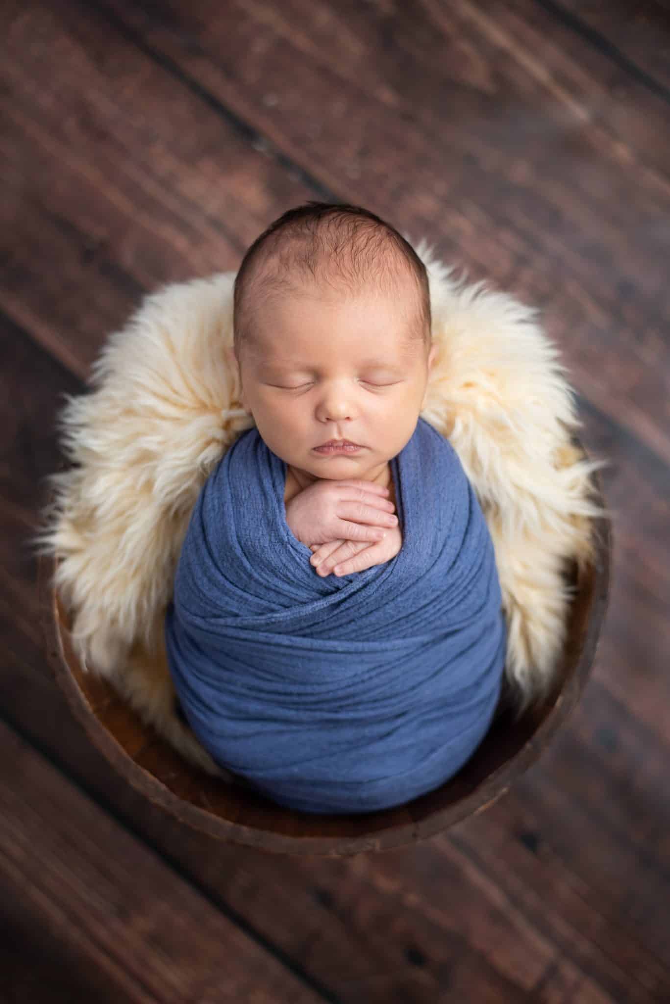 Peacefully sleeping newborn in a blue wrap and fur-lined basket at a Toronto newborn photography studio