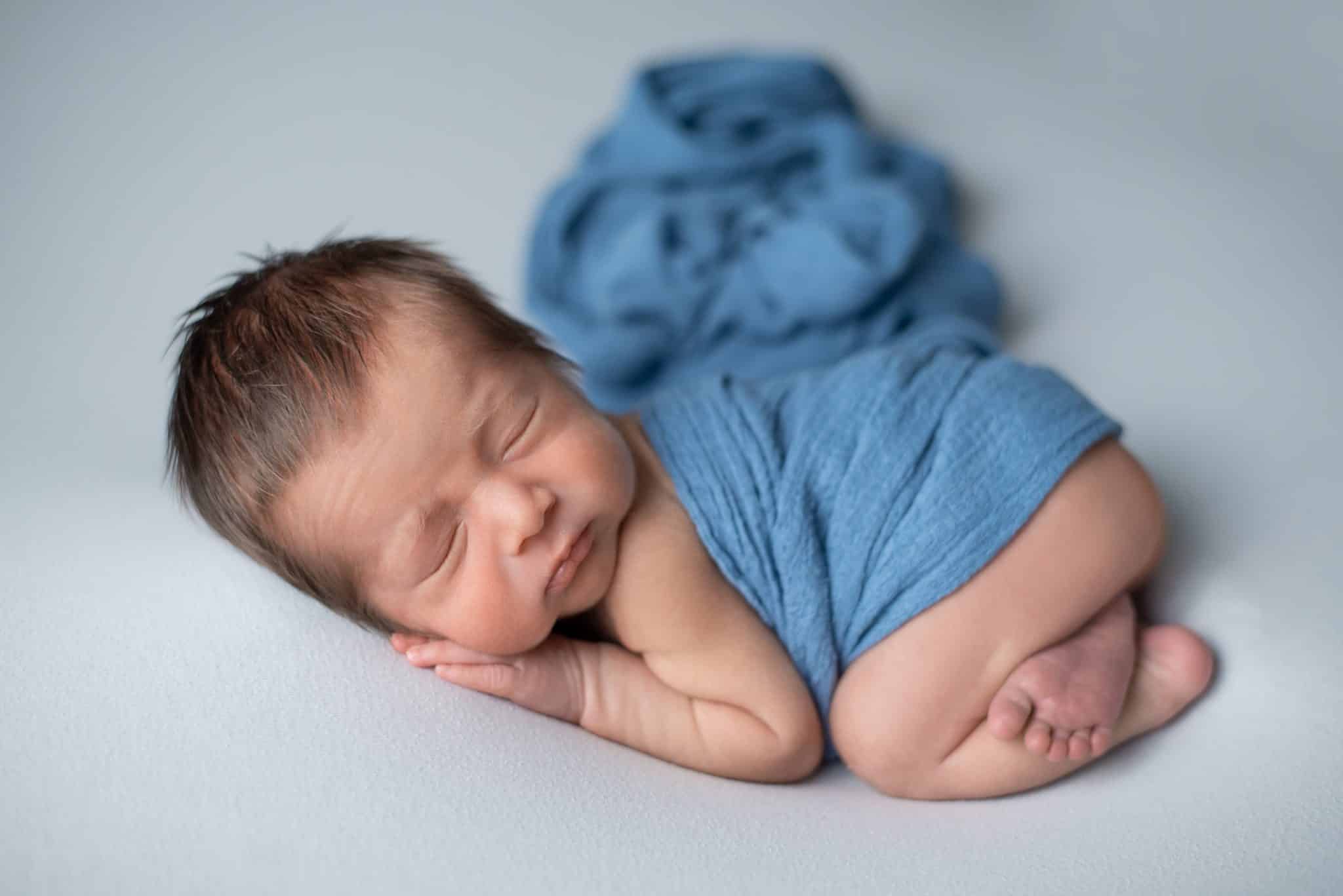 Cute newborn baby sleeping soundly in a blue outfit on a soft blue blanket, ideal for baby photography Mississauga.