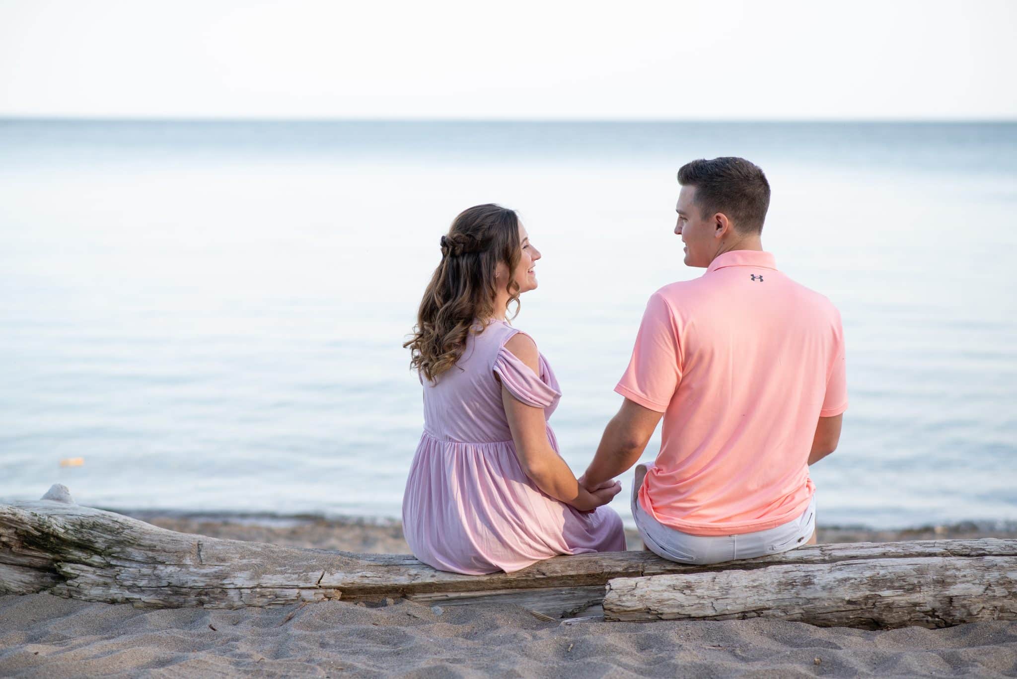 Relaxed maternity photography session by the lake, couple sitting together during sunset pregnancy photoshoot in Toronto outdoor location.