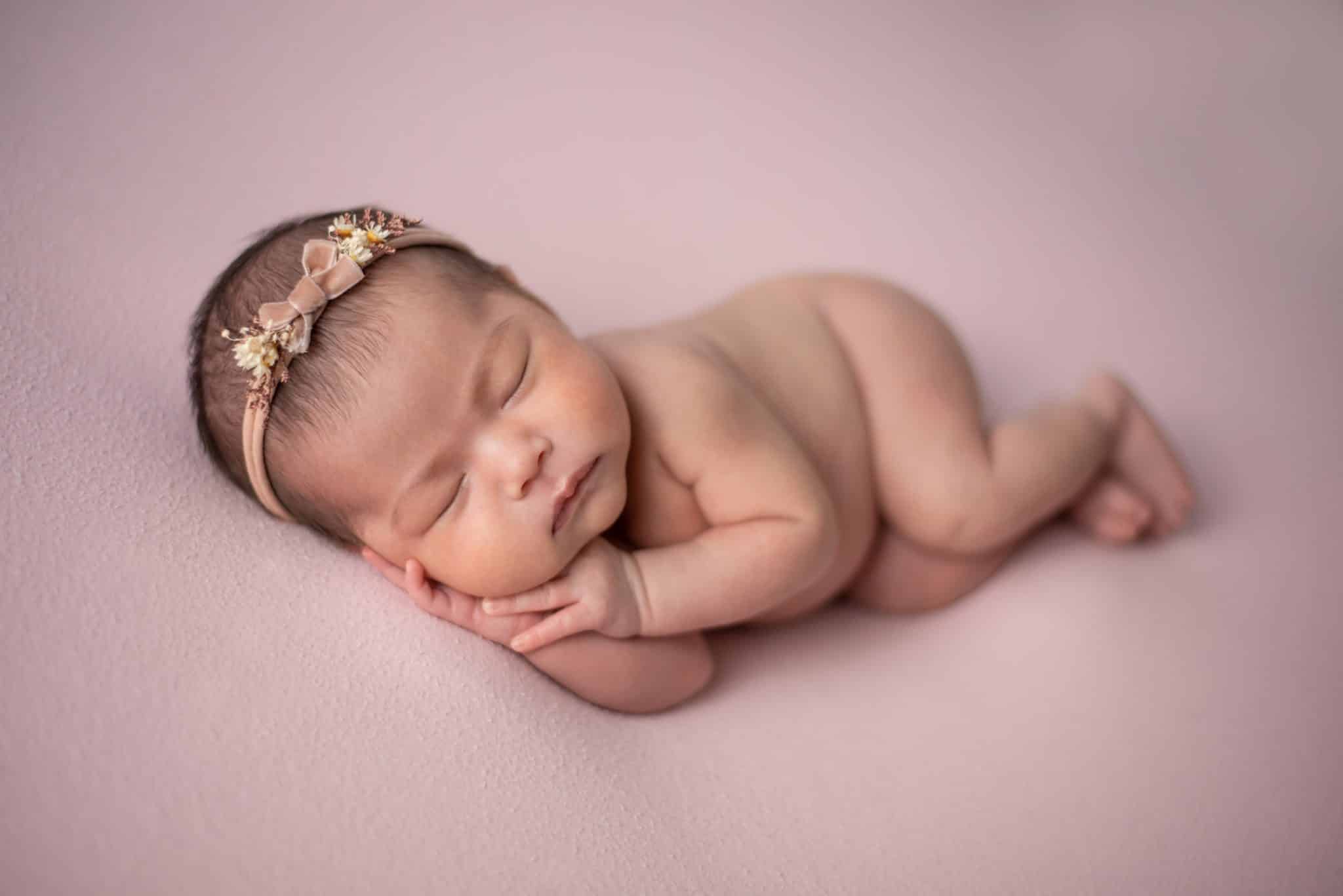 Sweet newborn baby girl sleeping on a soft pink blanket with a floral headband, captured by a professional newborn photographer Mississauga.