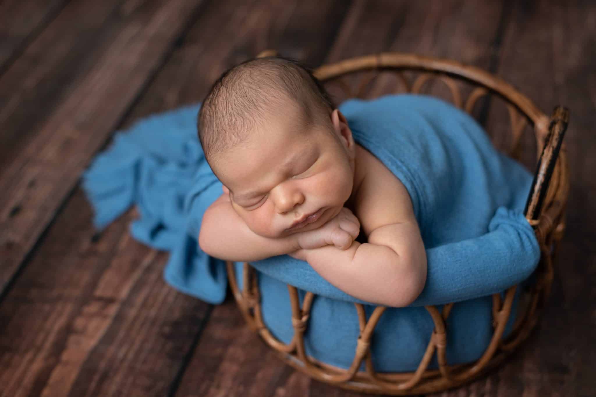Sleeping newborn baby resting in a woven basket with a soft blue wrap during a Toronto newborn photography session